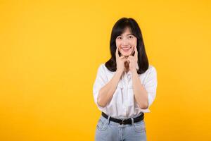 Young beautiful asian woman happy smile wearing white shirt and denim jean plants over yellow isolated background smiling confident showing and pointing with fingers teeth and mouth. Dental concept. photo