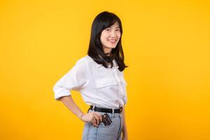 young fun woman of Asian ethnicity wear white shirt and denim jean hold put or pull credit bank card from pocket isolated on yellow background. Lifestyle online payment shopping concept. photo