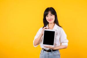 confidente asiático mujer abraza el digital edad, participación tableta en un vibrante amarillo antecedentes. moderno conectividad, conocimiento de la tecnología, y empoderamiento. digital estilos de vida y tecnológico avances foto