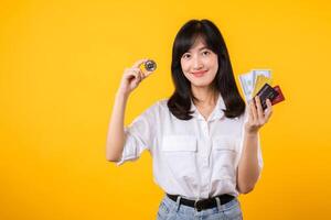 Capture the essence of digital currency with stunning portrait of young Asian woman confidently holds digital currency, cash, credit card, and smartphone. The digital currency concept. photo