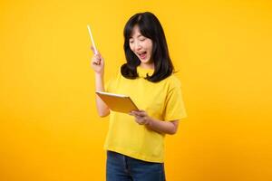 joven asiático mujer vistiendo amarillo camiseta y pantalones demostración contento sonrisa mientras utilizando digital tableta, mostrando pensativo expresión y creativo idea. educación tecnología innovador pensando concepto. foto