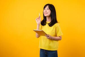 young Asian woman wearing yellow t-shirt and jeans showing happy smile while using digital tablet, displaying thoughtful expression and creative idea. education technology innovative thinking concept. photo