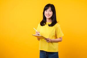 experiencia el alegría de educación tecnología con retrato. un joven asiático mujer vistiendo un amarillo camiseta y mezclilla pantalones vitrinas un contento sonrisa mientras utilizando digital tableta. educación tecnología concepto. foto