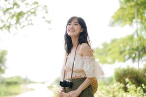 Portrait of asian young woman traveler with weaving hat and basket and a camera on green public park nature background. Journey trip lifestyle, world travel explorer or Asia summer tourism concept. photo