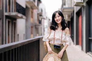 Happy youth asian woman with camera travels street city trip on leisure weekend. Young hipster female tourist sightseeing summer urban Bangkok destination. Asia summer tourism concept. photo