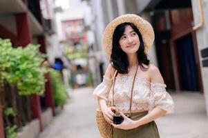 Happy youth asian woman with camera travels street city trip on leisure weekend. Young hipster female tourist sightseeing summer urban Bangkok destination. Asia summer tourism concept. photo