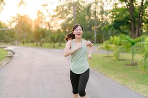 Fit Asian young woman jogging in park smiling happy running and enjoying a healthy outdoor lifestyle. Female jogger. Fitness runner girl in public park. healthy lifestyle and wellness being concept photo