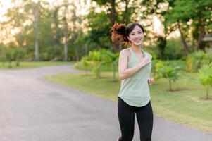 Fit Asian young woman jogging in park smiling happy running and enjoying a healthy outdoor lifestyle. Female jogger. Fitness runner girl in public park. healthy lifestyle and wellness being concept photo