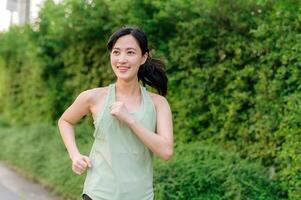 ajuste asiático joven mujer trotar en parque sonriente contento corriendo y disfrutando un sano al aire libre estilo de vida. hembra persona que practica jogging. aptitud corredor niña en público parque. sano estilo de vida y bienestar siendo concepto foto