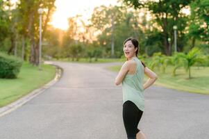 Fit Asian young woman jogging in park smiling happy running and enjoying a healthy outdoor lifestyle. Female jogger. Fitness runner girl in public park. healthy lifestyle and wellness being concept photo