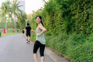 Fit Asian young woman jogging in park smiling happy running and enjoying a healthy outdoor lifestyle. Female jogger. Fitness runner girl in public park. healthy lifestyle and wellness being concept photo