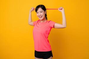 Portrait young asian sports fitness woman happy wearing pink sportswear and stretching resistance band doing exercise training workout against yellow background. wellbeing healthy lifestyle concept. photo