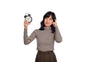 Portrait of thinking young Asian woman with sweater shirt holding alarm clock isolated on white background photo