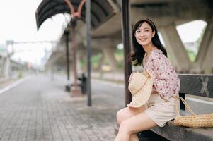 young asian woman traveler with weaving basket waiting for train in train station. Journey trip lifestyle, world travel explorer or Asia summer tourism concept. photo