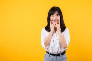 Young beautiful asian woman happy smile wearing white shirt and denim jean plants over yellow isolated background smiling confident showing and pointing with fingers teeth and mouth. Dental concept. photo