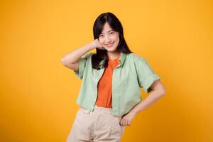 cheerful Asian woman 30s wearing green and orange shirt confidently holds hip with hands, showcasing poise and self-assurance. Perfect for capturing a sense of empowerment and modern fashion. photo