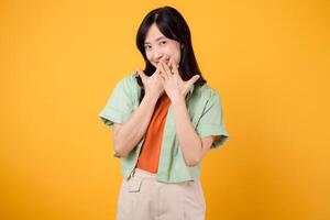 shy young asian woman 30s covering her mouth with hands isolated on yellow background. expression of embarrassment or uncertainty. shyness, embarrassment, and body language concept. photo