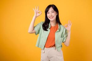 portrait beauty cheerful young asian woman happy smile showing okay hand sign gesture isolated on yellow background. positive attractive face confident success business concept. photo