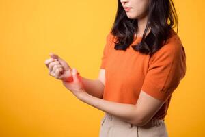 Young Asian woman in her 30s with wrist injury. holding her wrist and looking pained against yellow background. close-up perspective. wrist injuries, pain, inflammation, and medical care concept. photo