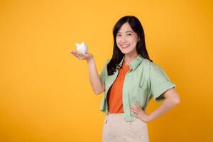portrait beauty attractive cheerful young asian 30s woman happy smile holding piggy saving bank isolated on yellow background. success wealth investment, economy money finance for retire concept. photo