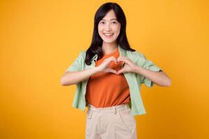 Close up of Asian woman 30s wearing orange shirt showing heart hand gesture, symbolizing affection and warmth. Perfect for expressing love and spreading positive vibes in various projects. photo