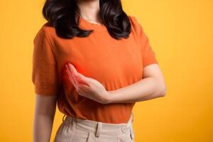 Woman hand checking lumps on her breast for signs of breast cancer on yellow background. Healthcare world health day concept. photo