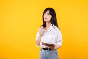 dudoso asiático joven adulto negocio mujer trabajando en digital tableta y mirando lejos pensando de solución aislado en amarillo fondo, considerando oferta, haciendo decisión o sensación duda concepto. foto