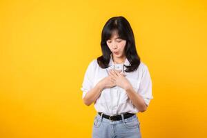 Happy young asian businesswoman wearing white shirt and denim jean holding cash, hugging dollars money and smiling, standing over yellow background. Love to be rich concept. photo