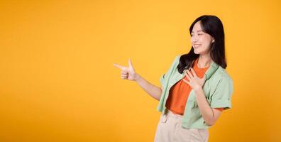 joven asiático mujer en su 30, vistiendo un verde camisa en un naranja camisa, señalando dedos a gratis Copiar espacio. explorar el mundo de descuento compras promociones con esta vibrante imagen. foto