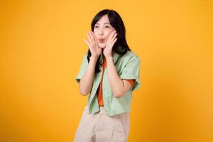 Energetic 30s Asian woman in a vibrant green and orange shirt, shouting with enthusiasm. Explore the concept of discount shopping promotion with this isolated yellow background photo. photo