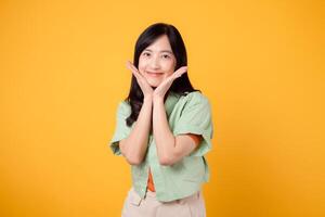 A young Asian woman in her 30s wearing a green shirt on an orange shirt radiates joy with a happy face. Discover the vibrant energy of cheerful image on a yellow background. photo