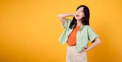 essence of happiness and well-being with cheerful young Asian woman in her 30s wearing an orange shirt. Her happy mind wellness gesture on yellow background illuminates compelling happiness portrait. photo