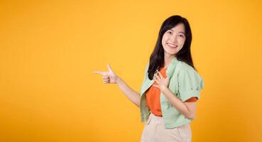 joven asiático mujer en su 30, vistiendo un verde camisa en un naranja camisa, señalando dedos a gratis Copiar espacio. descuento compras promociones concepto. foto