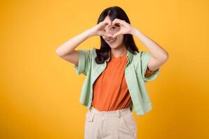 power of healthcare and wellness through an Asian woman in her 30s wearing a green shirt. Experience her heart hand gesture on a vibrant yellow background, capturing the essence of body wellness. photo