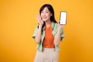 new mobile application with young Asian woman 30s, elegantly dressed in orange shirt and green jumper, using smartphone screen on yellow background. New mobile device and online shopping concept. photo