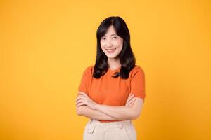 Unleash confident energy with a young Asian woman in her 30s, donning an orange shirt, showcasing crossed arm sign gesture on yellow background. photo