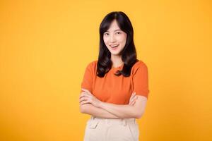 Step into confident grace with a young Asian woman in her 30s, wearing an orange shirt, displaying crossed arm sign gesture on yellow background. photo