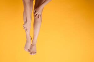 explorar piernas cuidado de la salud con un cerca arriba de mujer piernas, manos participación su dolorido piernas en un vibrante amarillo antecedentes. concepto de pierna dolor alivio. foto