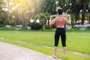 happiness of a fit Asian woman in her 30s, wearing pink sportswear, as she warms down after a sunset run in a public park. Embrace wellness living and the beauty of nature. photo