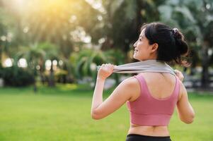 de cerca de un ajuste hembra persona que practica jogging como un asiático mujer en su 30, vistiendo rosado ropa de deporte, calienta abajo después un puesta de sol correr en un público parque. abrazo el concepto de bienestar vivo y naturaleza. foto