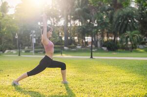 concept of wellness and well-being fit 30s young Asian woman in pink sportswear stretches muscles in park before run. healthy outdoor lifestyle with this fitness runner girl in a public park. photo