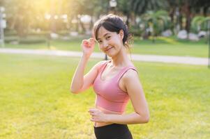 Experience the joy of wellness living as a happy young 30s Asian woman smiles at the camera in a park at sunset. Embrace the beauty of nature and a healthy lifestyle. photo