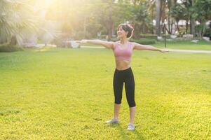 Female jogger. fit 30s young Asian woman in pink sportswear preparing warm up body in park before run. healthy outdoor lifestyle with fitness runner girl in sunset. concept of wellness and well-being photo