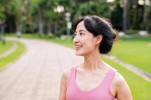 Woman jogger. young asian female happy smile wearing pink sportswear running in public park. Healthcare wellness concept. photo