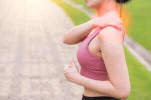 Woman jogger. young 30s asian female wearing pink sportswear holding her back pain after running exercise in public park. Pain in activity concept. photo