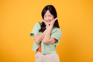 A young Asian woman in her 30s wearing a green shirt on an orange shirt radiates joy with a happy face. Discover the vibrant energy of cheerful image on a yellow background. photo