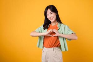 healthcare and wellness with an Asian woman 30s, wearing a green shirt. Witness her heart hand gesture on her chest against a yellow background, truly embracing the embodiment of body wellness. photo