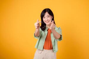 happiness with a young Asian woman in her 30s, dressed in an orange shirt and green jumper. Her mini heart gesture and gentle smile express a profound message through body language. photo