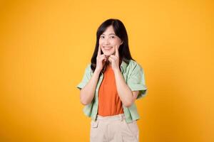 joven asiático mujer en su 30s vistiendo naranja camisa y verde saltador señalando a su dientes aislado en amarillo antecedentes. dental cuidado de la salud concepto. foto