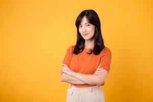 Confident young Asian woman in her 30s, wearing orange shirt, displays crossed arm sign gesture on yellow background. Hands gesture concept. photo